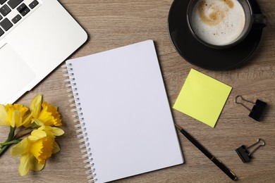 Photo of Notebook, other stationery, coffee, daffodils and laptop on wooden table, flat lay