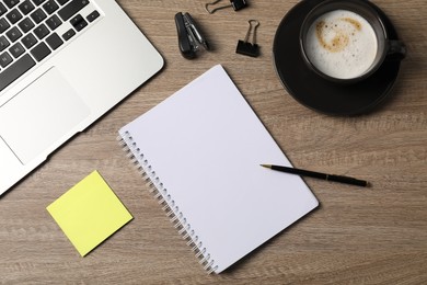 Photo of Notebook, other stationery, coffee and laptop on wooden table, flat lay
