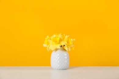 Photo of Beautiful daffodils in vase on white table against yellow background
