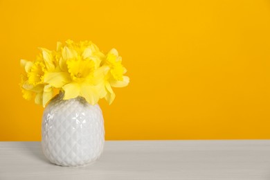 Photo of Beautiful daffodils in vase on white table against yellow background. Space for text