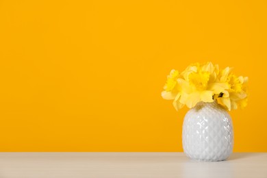 Photo of Beautiful daffodils in vase on white table against yellow background. Space for text