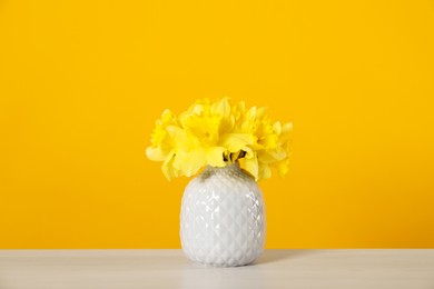 Photo of Beautiful daffodils in vase on white table against yellow background