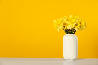 Photo of Beautiful daffodils in vase on white table against yellow background. Space for text