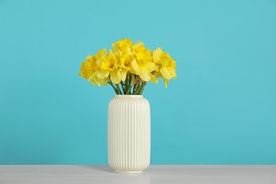 Photo of Beautiful daffodils in vase on light table against turquoise background