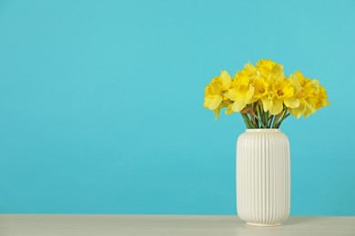 Photo of Beautiful daffodils in vase on table against turquoise background. Space for text