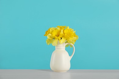 Photo of Beautiful daffodils in vase on grey table against turquoise background