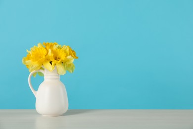 Photo of Beautiful daffodils in vase on table against light blue background. Space for text
