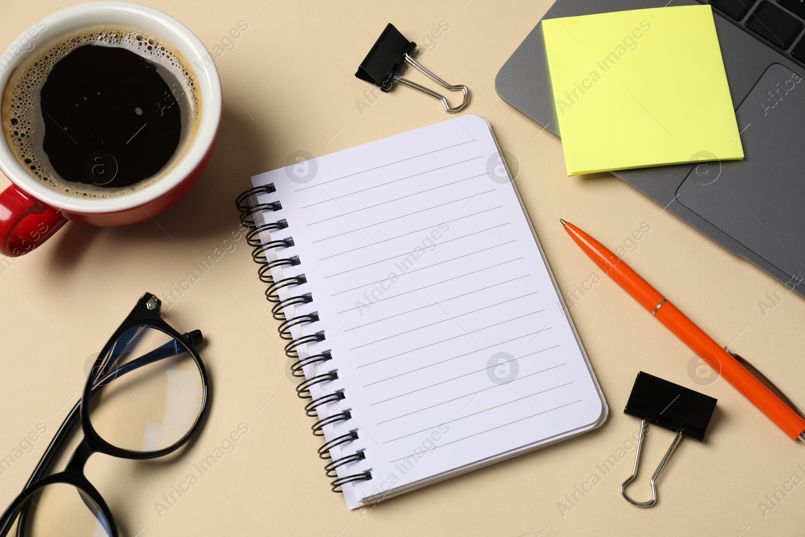 Notebook, pen, sticky note, binder clips, glasses, coffee and laptop on beige background, above view Photo of Notebook, pen, sticky note, binder clips, glasses, coffee and laptop on beige background, above view