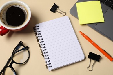 Photo of Notebook, pen, sticky note, binder clips, glasses, coffee and laptop on beige background, above view