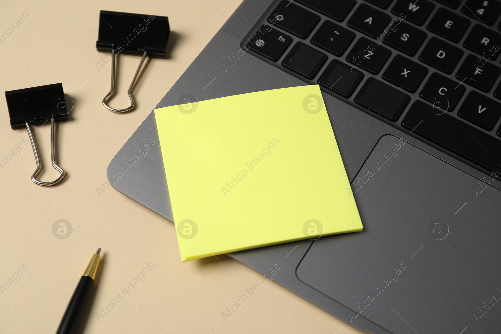 Sticky note, pen, binder clips and laptop on beige background, closeup Photo of Sticky note, pen, binder clips and laptop on beige background, closeup