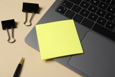 Photo of Sticky note, pen, binder clips and laptop on beige background, closeup