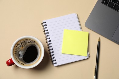 Photo of Notebook, sticky note, pen, coffee and laptop on beige background, flat lay