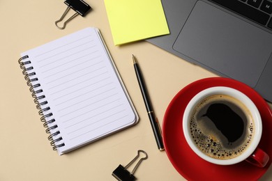 Photo of Notebook, sticky note, pen, binder clips, coffee and laptop on beige background, flat lay