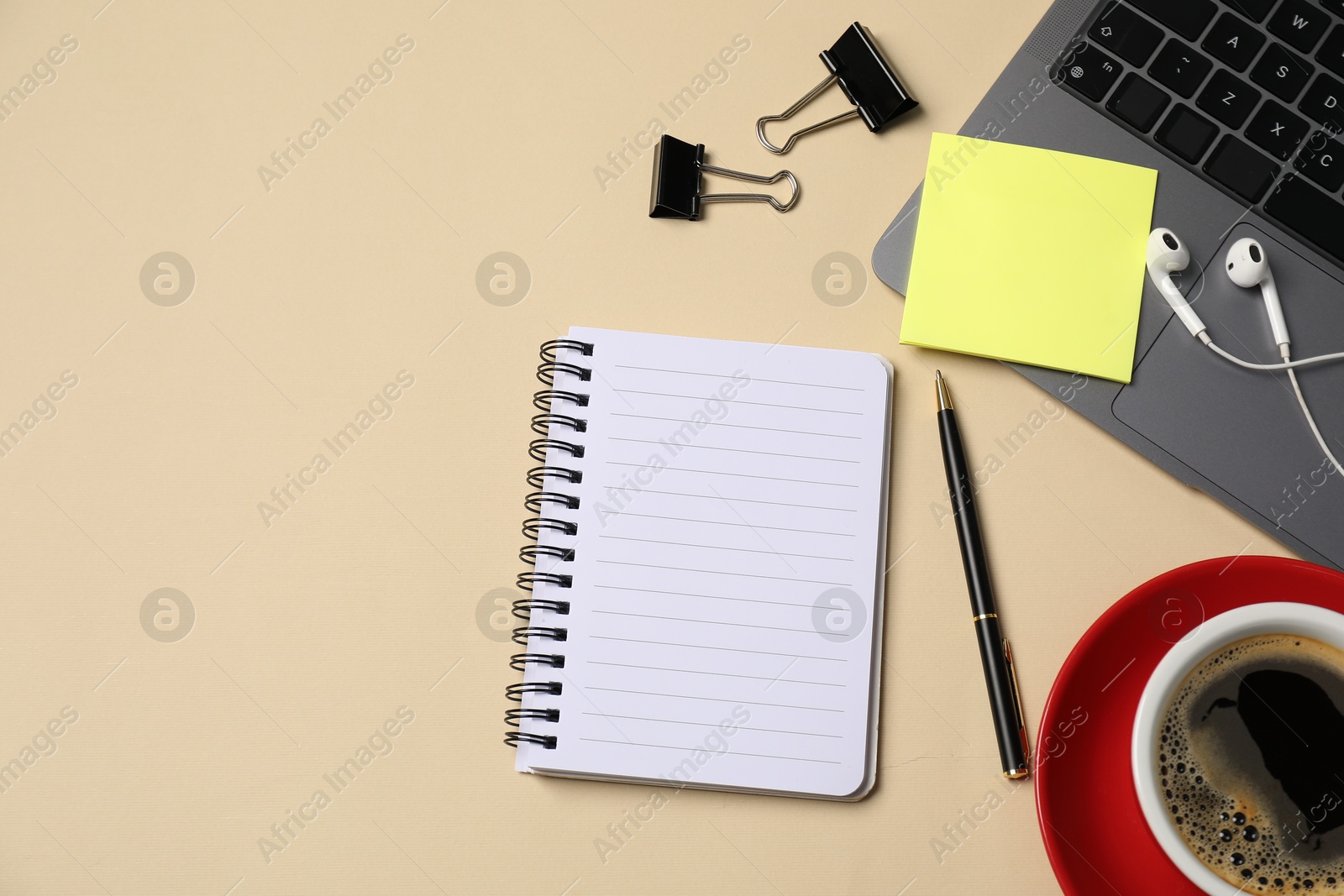 Photo of Notebook, sticky note, pen, binder clips, coffee, earphones and laptop on beige background, flat lay. Space for text