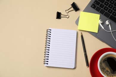 Photo of Notebook, sticky note, pen, binder clips, coffee, earphones and laptop on beige background, flat lay. Space for text