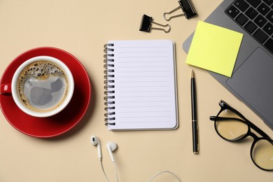 Photo of Notebook, sticky note, pen, binder clips, coffee, earphones, glasses and laptop on beige background, flat lay