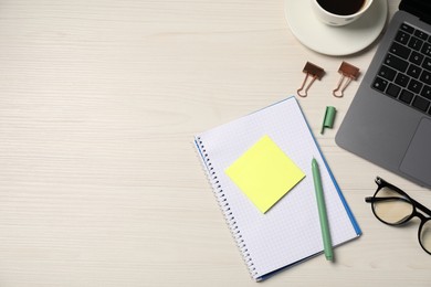 Photo of Notebook, sticky note, pen, glasses, binder clips and laptop on wooden table, flat lay. Space for text