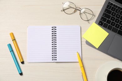 Photo of Notebook, sticky note, pen, markers, coffee, glasses and laptop on wooden table, flat lay