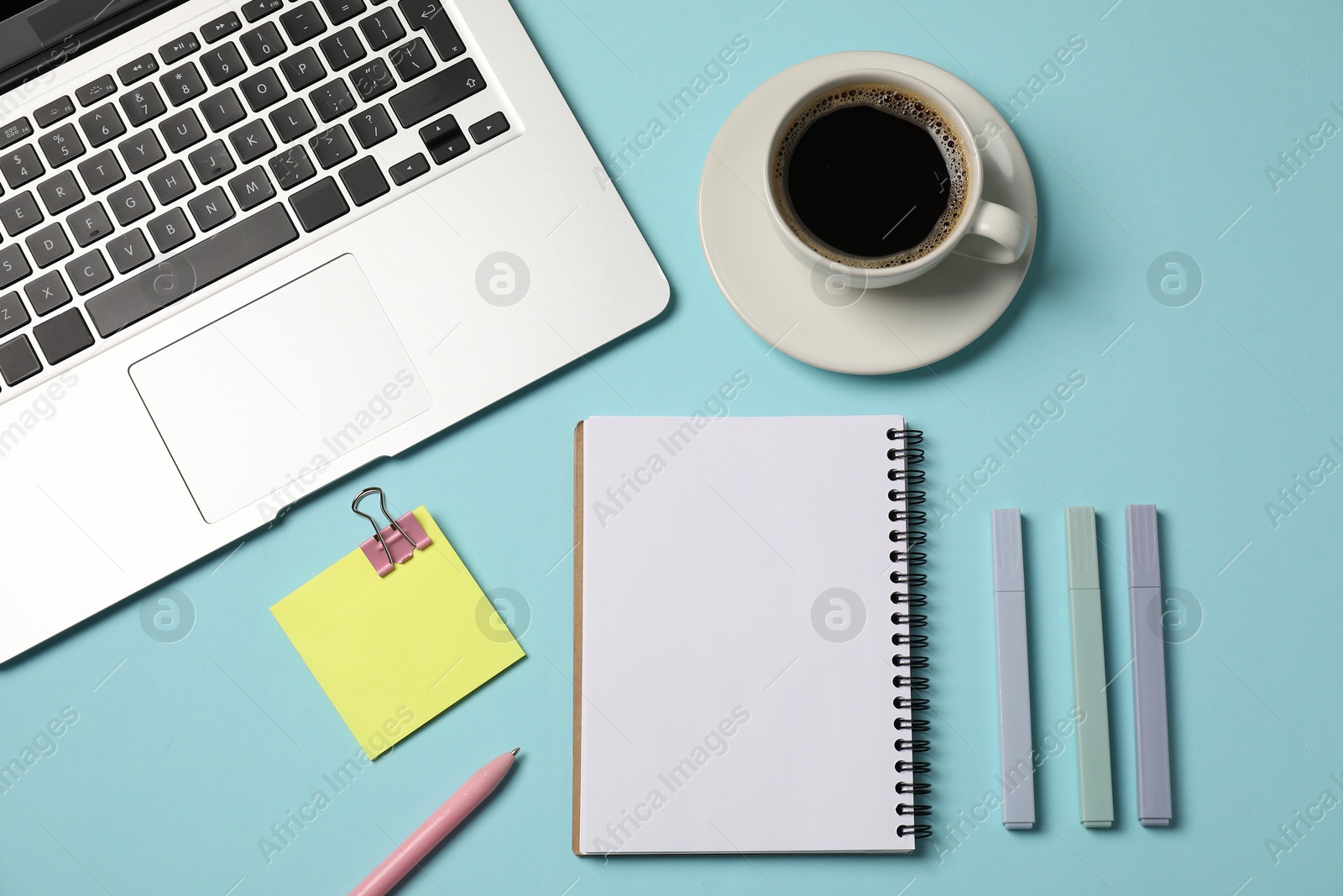 Photo of Notebook, other stationery, coffee and laptop on light blue background, flat lay