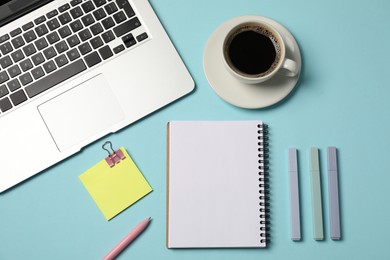 Photo of Notebook, other stationery, coffee and laptop on light blue background, flat lay