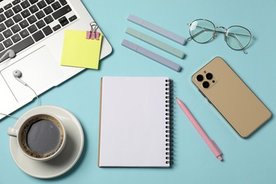 Photo of Notebook, other stationery, smartphone, coffee, glasses, earphones and laptop on light blue background, flat lay