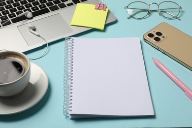 Photo of Notebook, other stationery, smartphone, coffee, glasses and laptop on light blue background, closeup