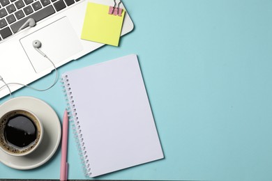 Photo of Notebook, pen, sticky note, earphones, coffee, binder clip and laptop on light blue background, flat lay. Space for text