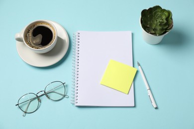 Photo of Notebook, sticky note, pen, glasses, coffee and floral decor on light blue background, above view