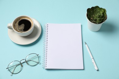 Photo of Notebook, pen, glasses, coffee and floral decor on light blue background, above view