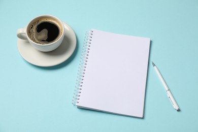 Photo of Notebook, pen and coffee on light blue background, above view