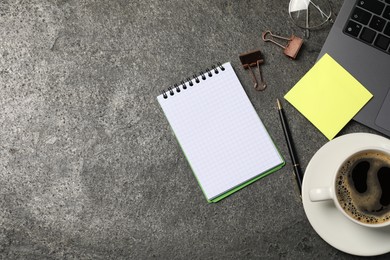 Photo of Notebook, pen, sticky note, coffee, binder clips, and laptop on grey table, flat lay. Space for text