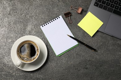 Photo of Notebook, pen, sticky note, coffee, binder clips, and laptop on grey table, flat lay