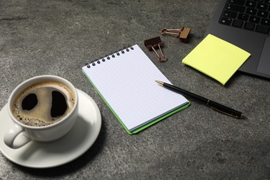 Photo of Notebook, pen, sticky note, coffee, binder clips, and laptop on grey table, closeup