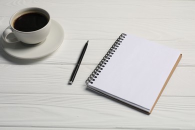 Photo of Notebook, pen and coffee on white wooden table, closeup