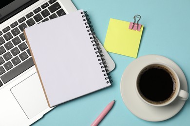 Photo of Notebook, sticky note, pen, coffee and laptop on light blue background, flat lay