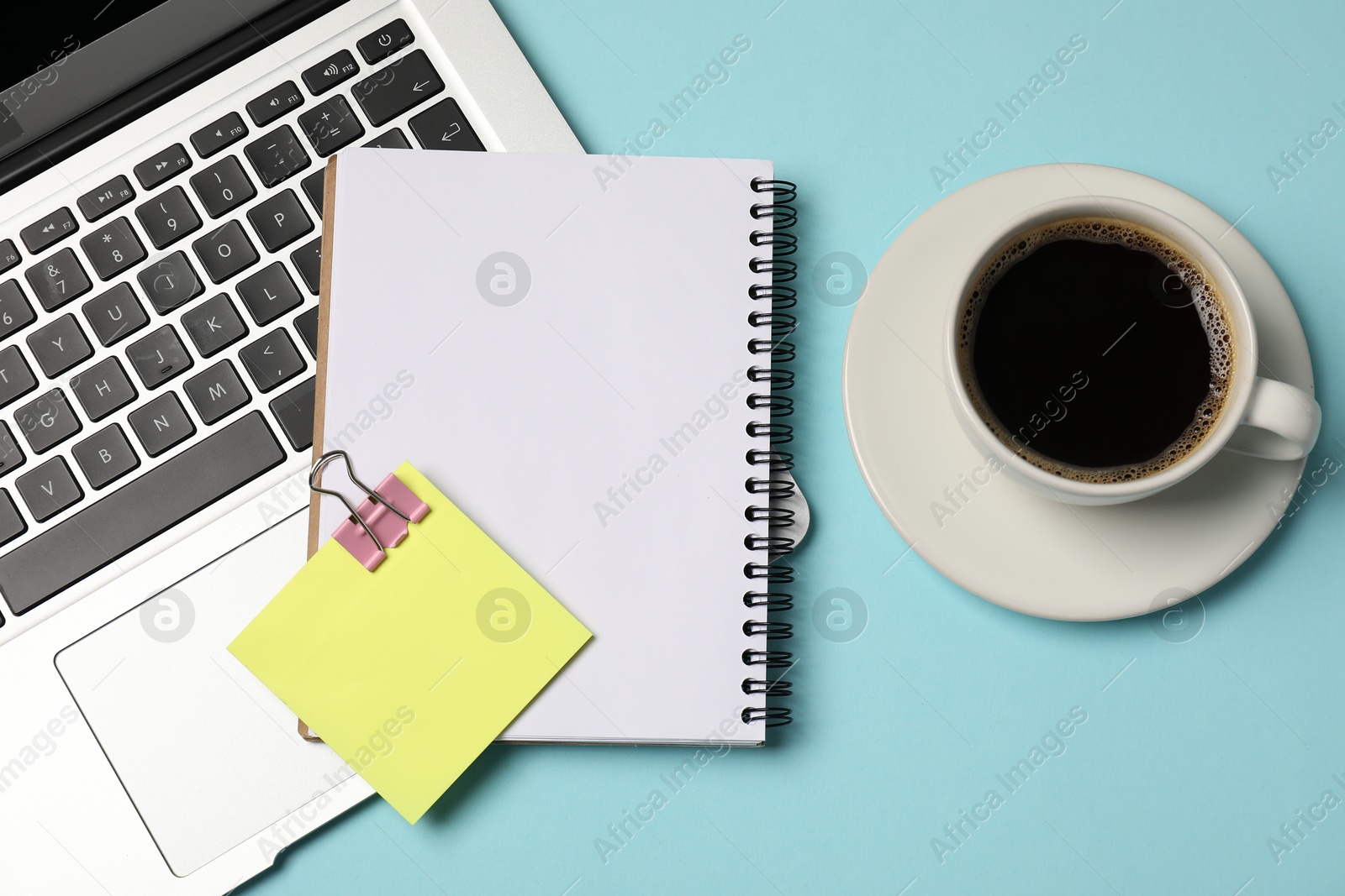 Photo of Notebook, sticky note, coffee and laptop on light blue background, flat lay