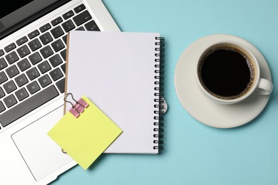 Photo of Notebook, sticky note, coffee and laptop on light blue background, flat lay