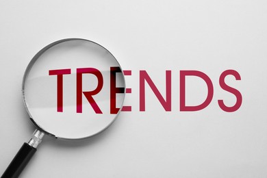 Image of Word Trends and magnifying glass on white background, top view