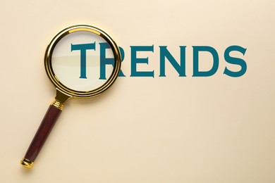 Image of Word Trends and magnifying glass on beige background, top view