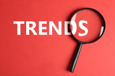 Image of Word Trends and magnifying glass on red background, top view