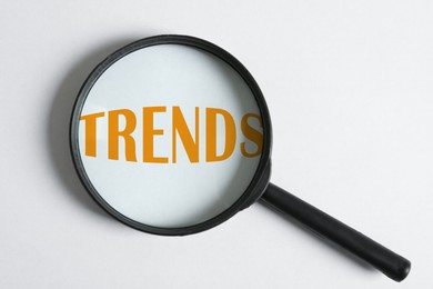Image of Word Trends and magnifying glass on white background, top view