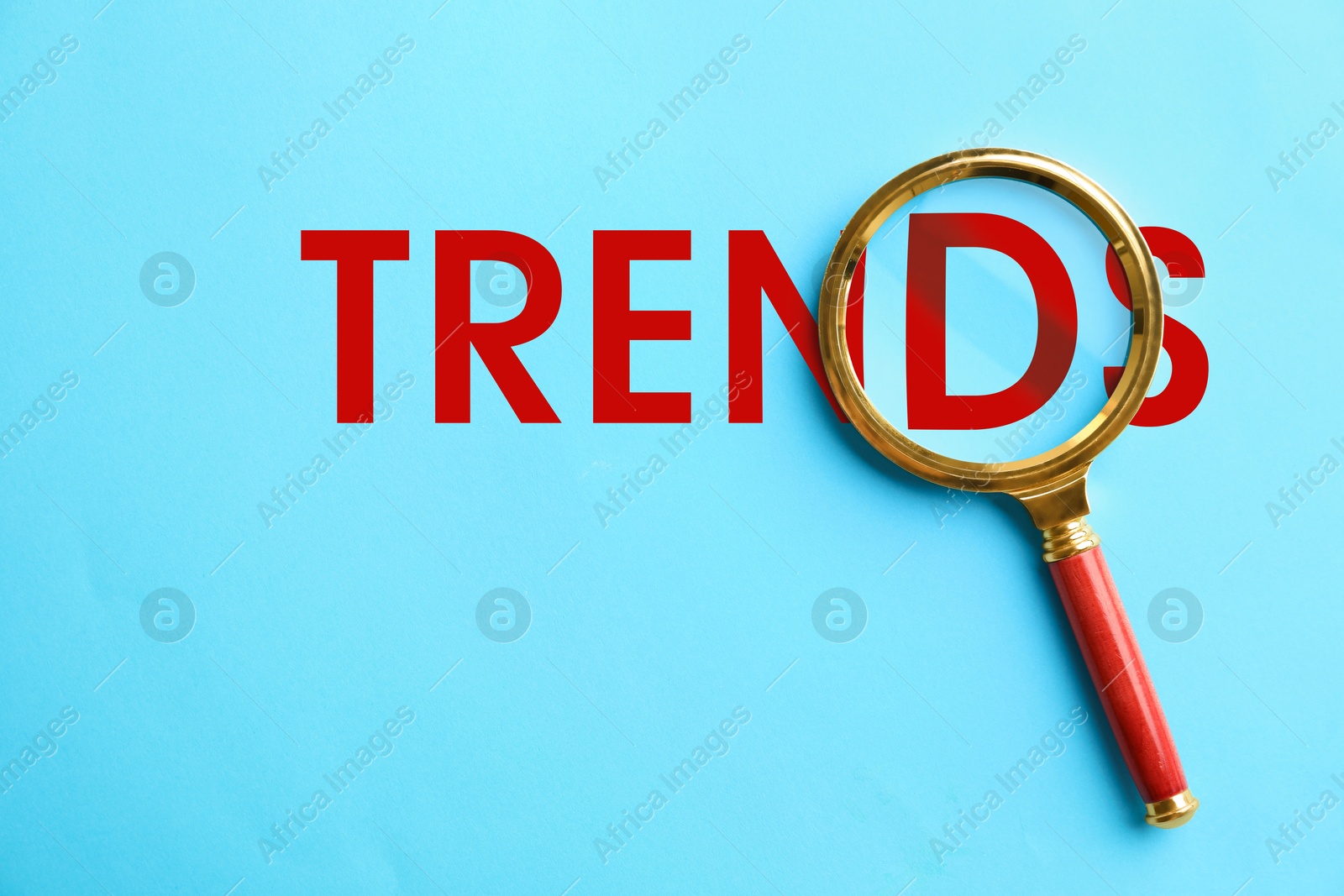Word Trends and magnifying glass on light blue background, top view Image of Word Trends and magnifying glass on light blue background, top view