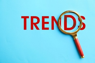 Image of Word Trends and magnifying glass on light blue background, top view