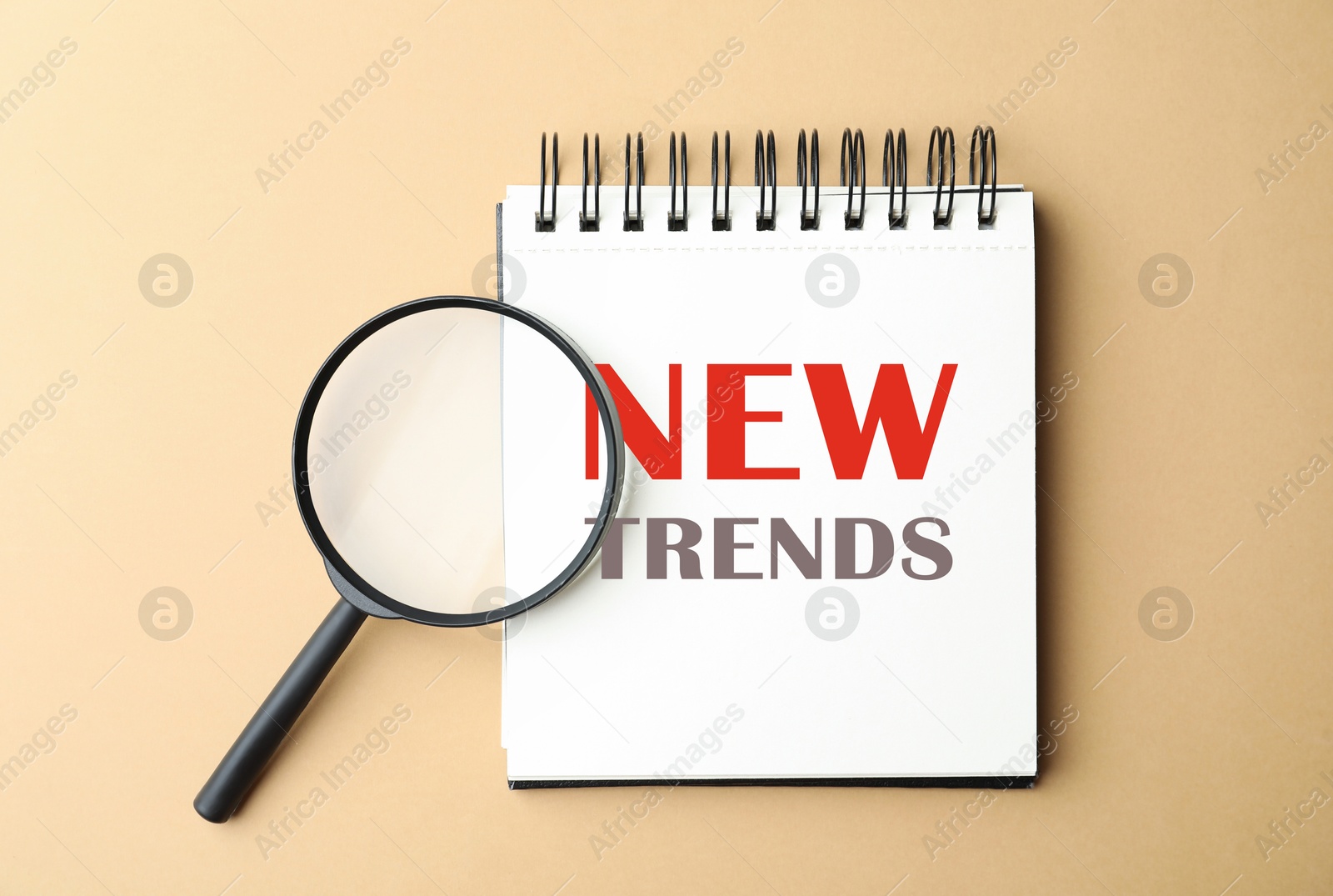 New Trends inscription in notebook and magnifying glass on beige background, top view Image of New Trends inscription in notebook and magnifying glass on beige background, top view