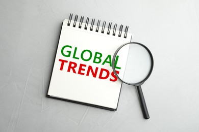 Image of Global Trends inscription in notebook and magnifying glass on light grey background, top view