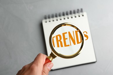 Image of Word Trends in notebook, view through magnifying glass in woman's hand