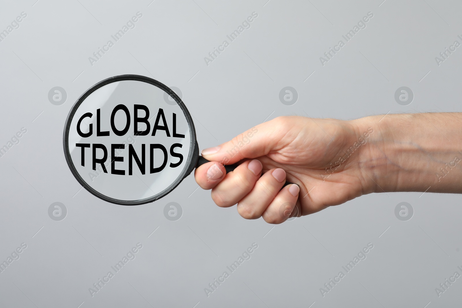 Woman holding magnifying glass with words Global Trends inside on light grey background, closeup Image of Woman holding magnifying glass with words Global Trends inside on light grey background, closeup
