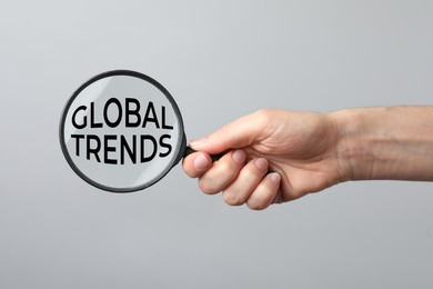 Image of Woman holding magnifying glass with words Global Trends inside on light grey background, closeup