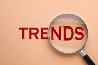Image of Word Trends and magnifying glass on dark beige background, top view