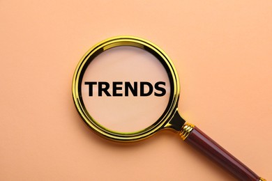 Image of Word Trends and magnifying glass on dark beige background, top view